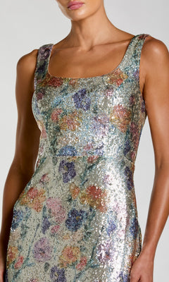 A woman wearing the Mac Duggal 56388 Long Formal Dress, a sleeveless gown with a square neckline, adorned with multicolored sequins and accented by a striking floral embellishment.