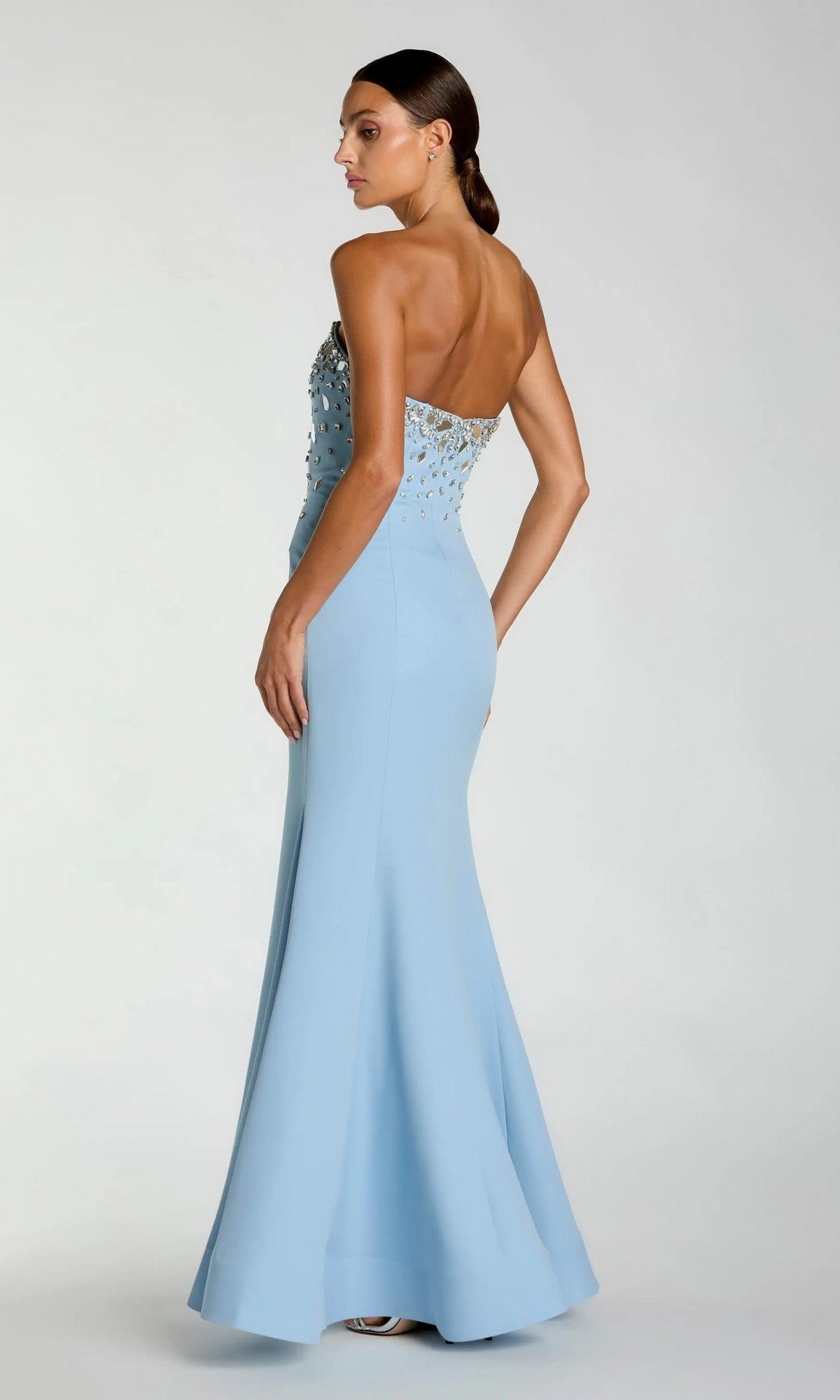 A woman wears the Mac Duggal 56393 long formal dress—a strapless, light blue mermaid gown with a fitted silhouette and intricate beaded detailing on the bodice—standing and looking to the side against a plain background.