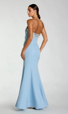 A woman wears the Mac Duggal 56393 long formal dress—a strapless, light blue mermaid gown with a fitted silhouette and intricate beaded detailing on the bodice—standing and looking to the side against a plain background.