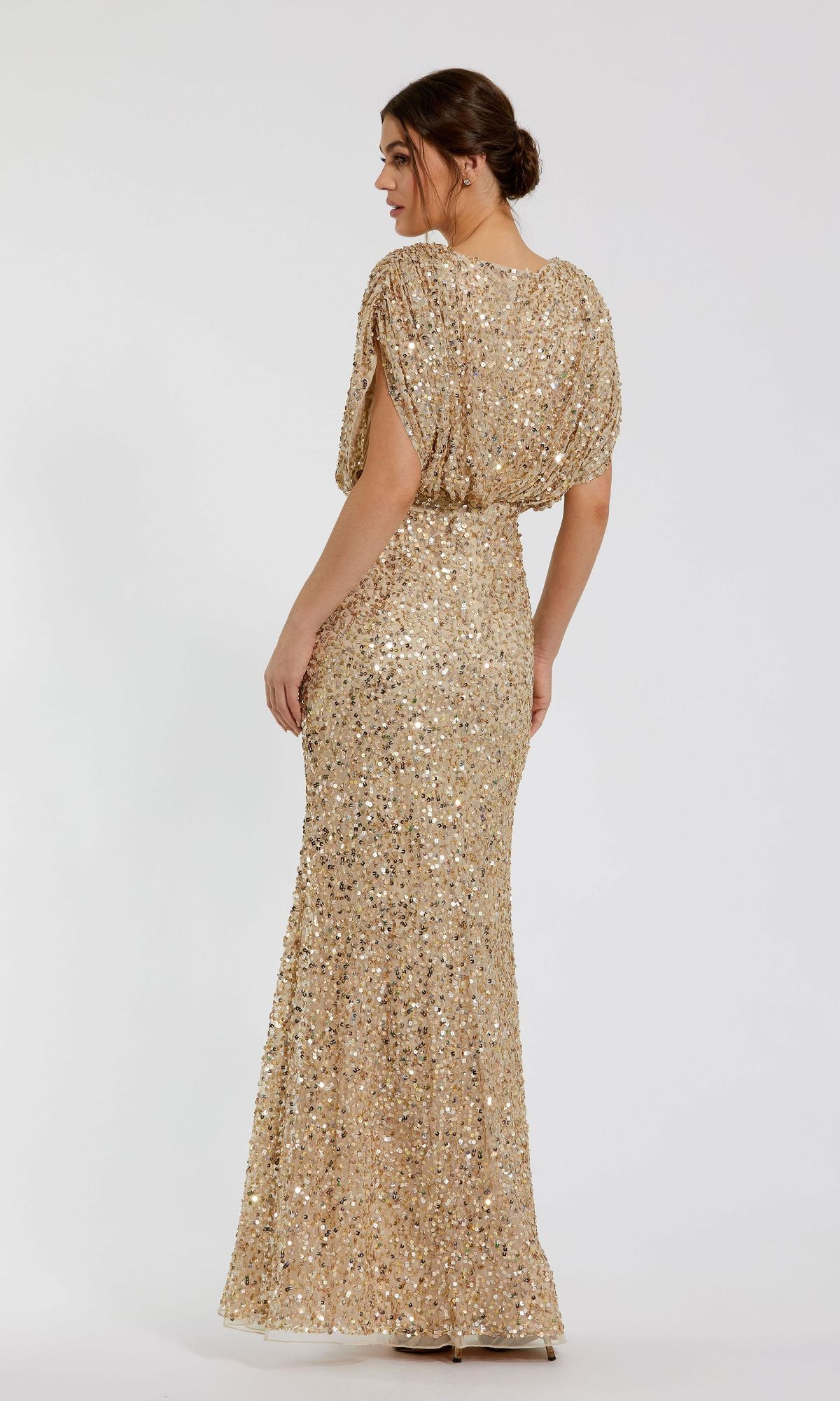 A woman models the Mac Duggal 5640 Short Sleeve Long Sequin Formal Dress, featuring a fitted silhouette and floor-length gold design, against a plain white background.