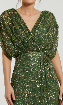 A person wears the Mac Duggal 5640 Short Sleeve Long Sequin Formal Dress, featuring a green sequin design, deep V-neckline, and gathered waist.