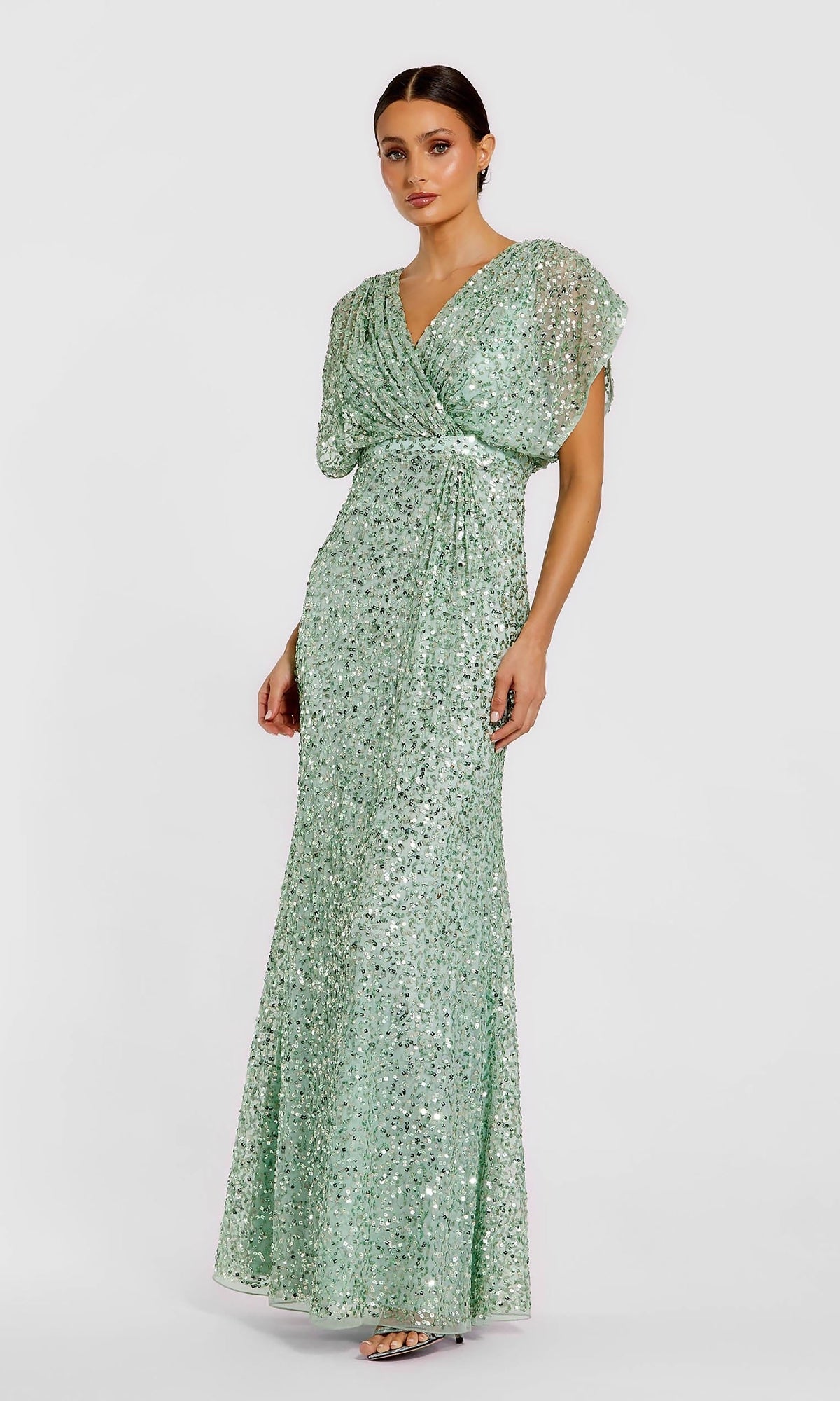 A woman poses against a plain light background wearing the Mac Duggal 5640 Short Sleeve Long Sequin Formal Dress in mint green, featuring flutter sleeves and a V-neckline.