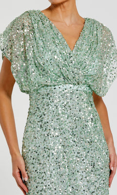 A person wearing the Mac Duggal 5640 Short Sleeve Long Sequin Formal Dress in light green, featuring a V-neck, gathered waist, and sparkling sequins.