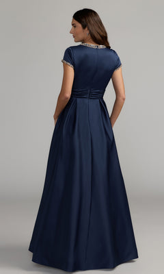 A woman stands facing away against a plain background, wearing the Long Formal Dress: Mac Duggal 56402—a floor-length, short-sleeve navy gown with jeweled trim that evokes timeless elegance.