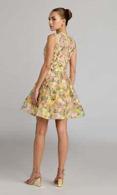 Model in profile gazes over her shoulder, showcasing the Mac Duggal 56409 Short Party Dress—a sleeveless yellow floral lace mini dress with a flattering fit-and-flare silhouette—paired with beige heels against a plain background.