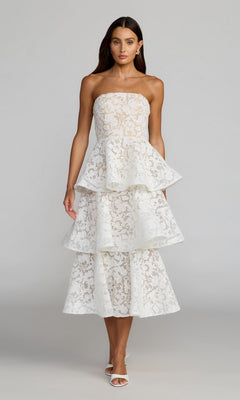 A woman models the Tea-Length Party Dress: Mac Duggal 56419 in ivory—a strapless lace design featuring a ruffled A-line skirt that falls to mid-calf—paired with white heels against a plain light gray background.