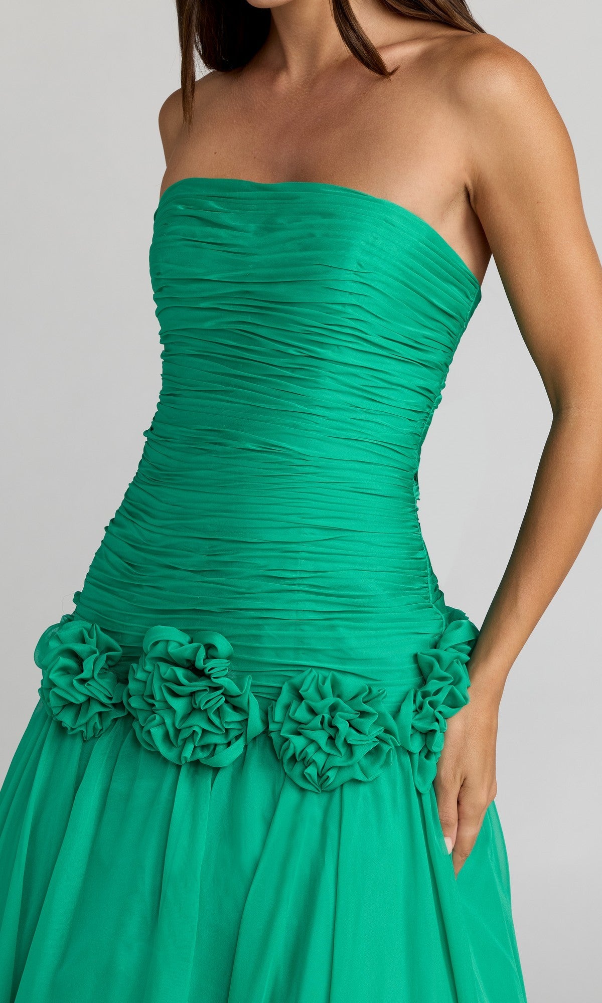A woman wearing the Mac Duggal 56428 long formal dress—a strapless, ruched green gown featuring a drop waist and three ruffled flower accents at the waist.