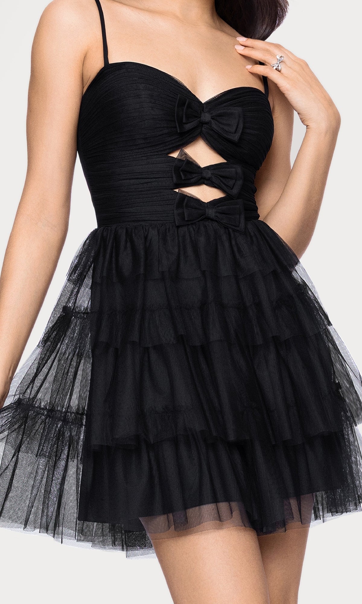 A woman wearing the Blondie Nites 5643BN short cut-out hoco dress, featuring a sleeveless design, tiered tulle skirt, and three bow accents on the bodice.