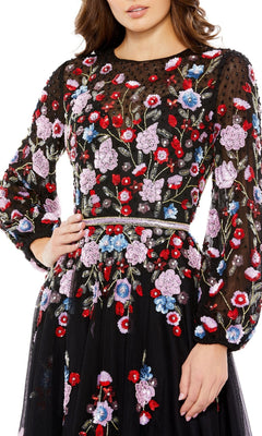 A woman wears the Mac Duggal Short Semi-Formal Dress 5712, a black long sleeve dress with red, purple, pink, and blue floral embroidery, delicate beading, and a beaded waist—ideal for semi-formal occasions.