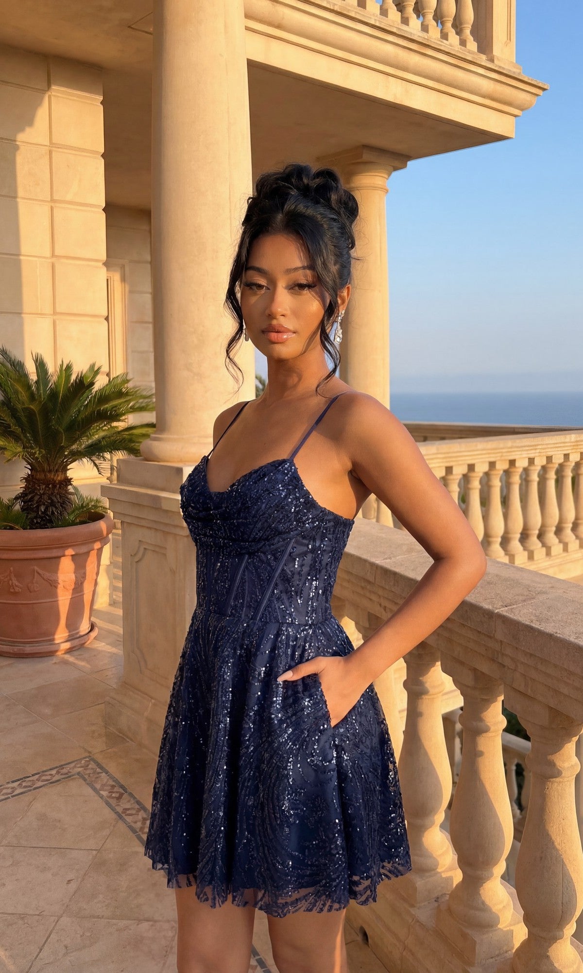 A woman in the Cowl-Neck Short Hoco Dress: Blondie Nites 5713BN poses on an ornate balcony with stone railings and columns, taking in a scenic outdoor view.