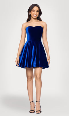 A woman models the Blondie Nites 5718BN short velvet hoco dress in royal blue, featuring a strapless, flared skirt style with black strappy heels, posed against a light background.