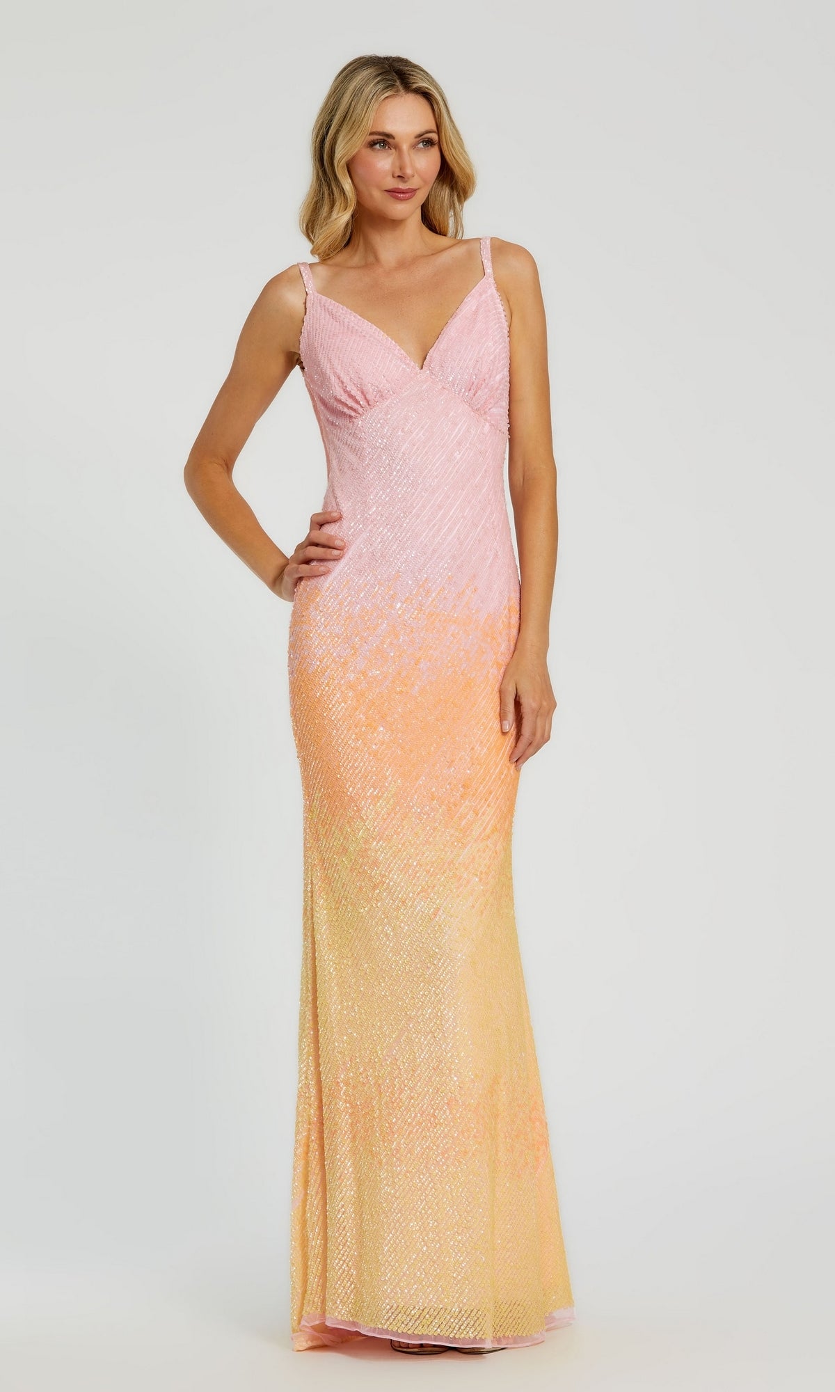 A woman models the Long Formal Dress 5763 by Mac Duggal—a sleeveless, floor-length ombre gown in pink, peach, and yellow with a chic cowl open back—against a plain light background.