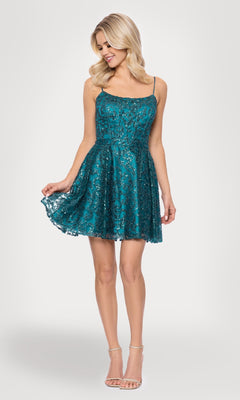 A woman models the Mini Teal Glitter Hoco Dress: Blondie Nites 5802BN, featuring sparkly lace and thin straps, paired with nude heels while holding out the skirt hem against a plain light background.