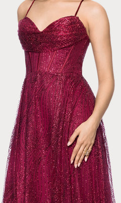 A person wearing the Blondie Nites 5814BN long prom dress in wine red, featuring glitter fabric, a sleeveless fitted style, sweetheart neckline, and thin straps, stands with one hand near their waist.