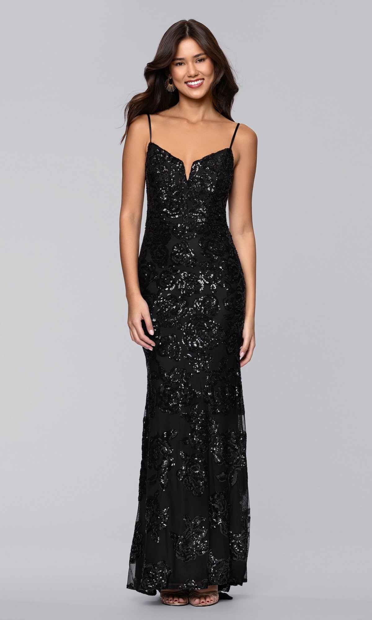 A woman wears the Blondie Nites 5905BN long prom dress, a form-fitting, floor-length black sequin gown with floral patterns, standing against a plain gray background.