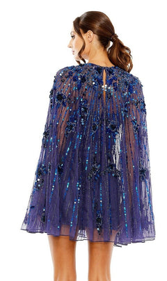 A woman with brown hair in a low ponytail is seen from the back wearing the Mac Duggal 5917 Beaded-Cape Short Hoco Dress, featuring a sheer blue sequin and floral-applique cape layered over a beaded cocktail dress.
