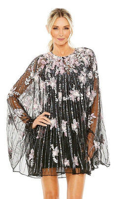 A woman wearing the Mac Duggal 5917 Beaded-Cape Short Hoco Dress, featuring a black short design with a sheer cape overlay embellished with pink and white floral embroidery, stands against a white background.
