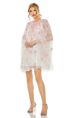 Woman wearing the Beaded-Cape Short Hoco Dress by Mac Duggal 5917— a sheer white dress with pink floral embroidery—paired with silver high-heeled sandals, standing against a plain white background.
