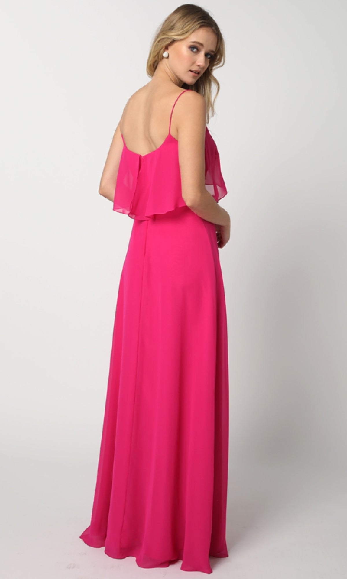 A woman models the Juliet 591, a bright pink floor-length wedding-guest dress with spaghetti straps and ruffled pop-over bodice, against a light background.
