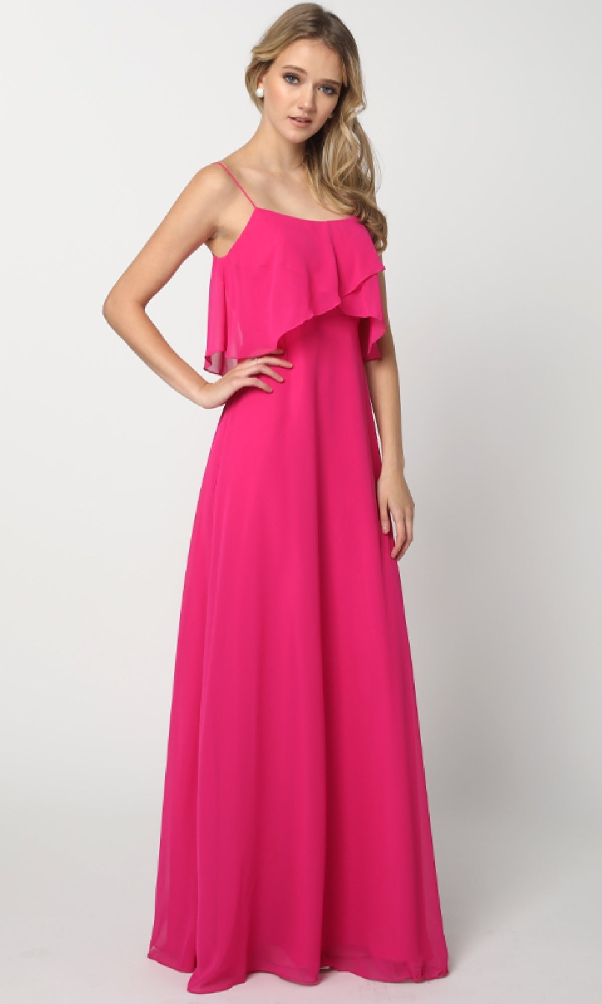A woman wears the Juliet 591 long wedding-guest dress, featuring a sleeveless pop-over bodice and ruffled overlay in hot pink, standing against a plain white background.