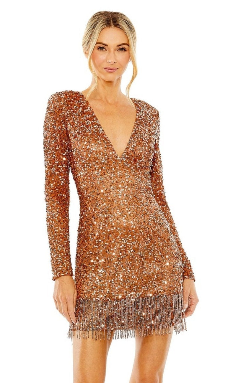 A woman stands against a white background wearing the Mac Duggal 5928 short beaded copper homecoming dress, which features a fitted long-sleeve design, deep V-neckline, and fringe detail at the hem.
