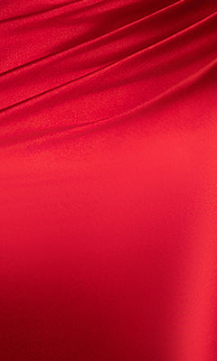 A close-up of smooth, shiny red fabric with diagonal folds and a silky texture, reminiscent of the Blondie Nites 5946BN Long Prom Dress with its fitted skirt and elegant corset bodice.