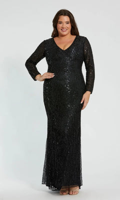 A woman stands smiling against a plain, light background, wearing the Mac Duggal 5947 Long Plus-Size Formal Dress in black—a floor-length, long-sleeved sequin gown with a V-neckline—paired with nude sandals; this stunning dress is perfect for special occasions.