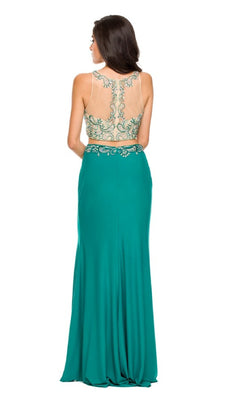 A woman stands facing away, wearing the Juliet 595 long prom dress—a sleeveless, floor-length green gown with a beaded top, sheer back, and intricate silver embroidery.