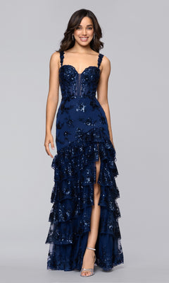 A woman stands against a plain gray background wearing the Blondie Nites 5962BN long prom dress in navy blue, featuring sequins, floral patterns, and a tiered ruffle skirt.
