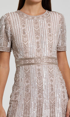 A woman wearing the Midi Fringe Wedding-Guest Dress: Mac Duggal 5980, a light pink short sleeve midi dress with intricate beadwork, sequins, and geometric patterns; shown from shoulders to mid-thigh.