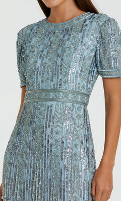 A woman wearing the Mac Duggal 5980 Midi Fringe Wedding-Guest Dress, a fitted light blue short sleeve dress with geometric and floral bead and sequin embroidery.