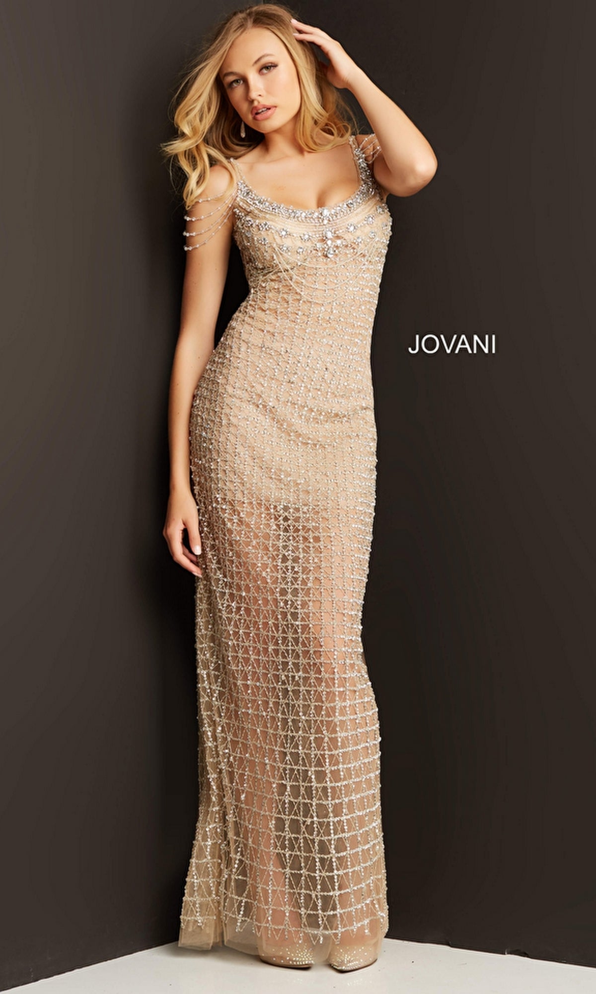 A woman in the Long Prom Dress by Jovani 05997—featuring nude fabric, crystal embellishments, and an open back—stands against a dark background with 
