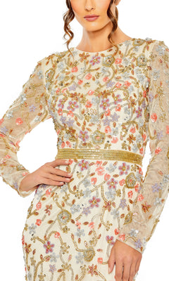 A woman models the Long Formal Dress 6016 by Mac Duggal, featuring a cream nude hue, sheer long sleeves, intricate floral embroidery with gold detailing, and a gold waistband. Her face is partly visible and one hand is on her hip.