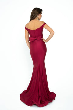 Woman wearing the Atria Off-the-Shoulder Long Formal Dress 6016H in burgundy with waist bow detailing, standing against a plain white background—an elegant option for prom or evening occasions.