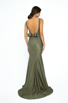 Model in the Atria Open-Back Sleeveless Long Prom Dress 6024H, floor-length and olive green with a low back and large bow detail, poses against a plain white background.