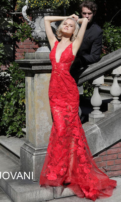 A woman in a red, floor-length Jovani Embroidered Long Prom Dress with Sequins featuring floral embroidery and a deep V-neckline stands on stone steps beside a man in a black suit.