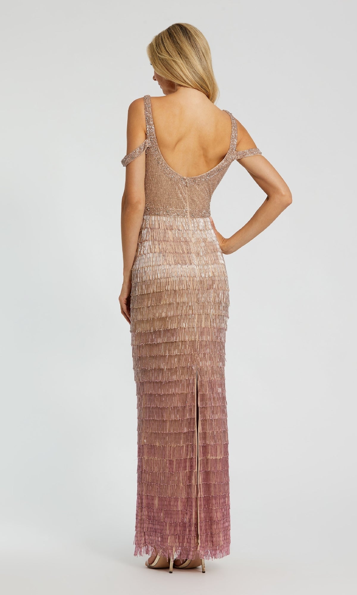 A woman stands facing away, wearing the Mac Duggal 6032 Fringed Pink Ombre Formal Dress with layered fringe in gradient beige to mauve and an open back.