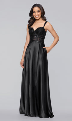 A woman wears the Long Prom Dress: Blondie Nites 6088BN in black, featuring an A-line satin silhouette, sequin-embellished bodice, thin straps, and a flowing skirt, standing against a plain gray background.