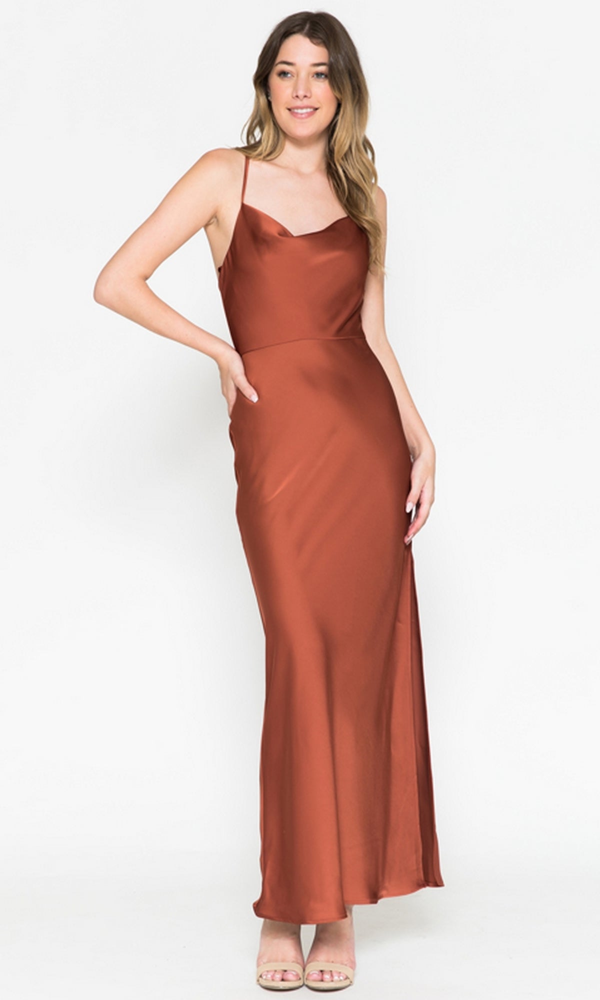 A woman stands smiling in a rust-colored Cowl-Neck Simple Tea-Length Satin Dress 6115 with spaghetti straps and beige open-toe heels, set against a plain white background.