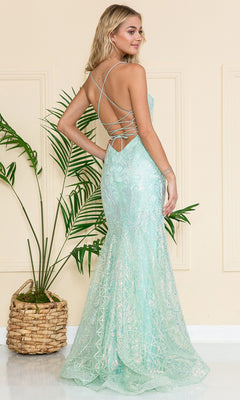 A woman in the Iridescent Long Embellished Prom Dress 6116, featuring light blue fabric, crisscross straps, and a backless design, stands near a potted plant.