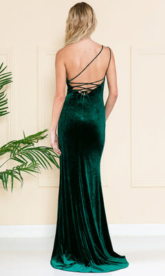 Someone stands indoors near a plant wearing the One-Shoulder Long Velvet Formal Dress 6118, featuring a floor-length, dark green design with an elegant lace-up back.