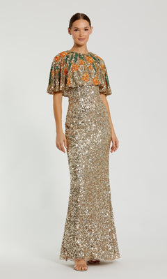 A woman models the Caped Gold Sequin Formal Gown (Mac Duggal 6120) featuring a long gold sequin design and a green-orange embellished capelet, posing against a plain white background.