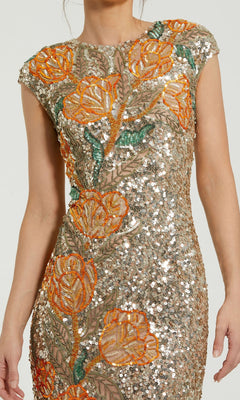 A woman wearing the Mac Duggal 6121 long formal dress, featuring orange and green floral embroidery with sequin embellishments on a beige mesh background.