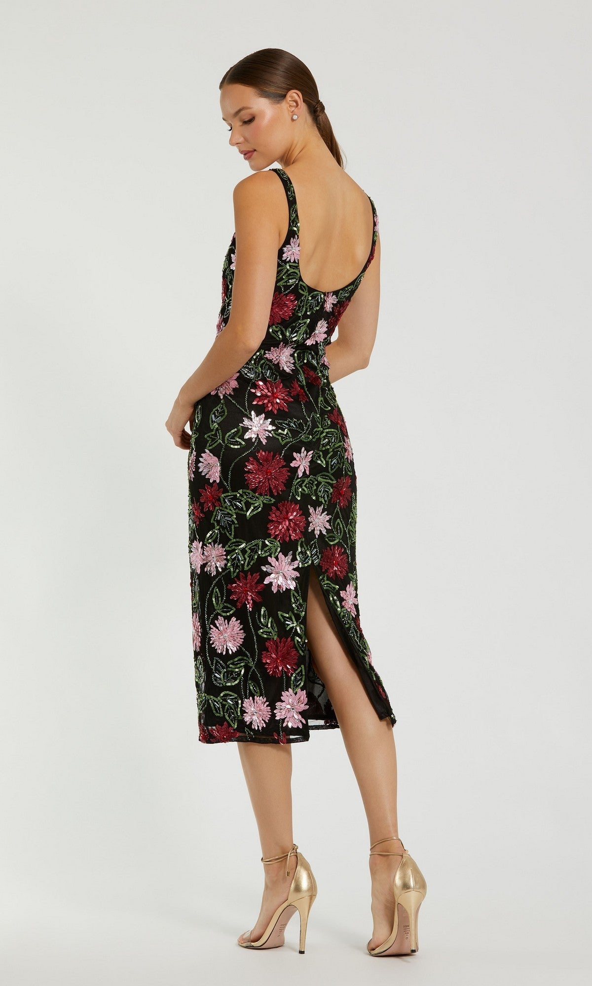 A woman stuns in the Mac Duggal 6124 Beaded Midi Wedding Guest Dress, featuring a sleeveless, backless design with floral beaded embroidery and a back slit, paired with gold high-heeled sandals.