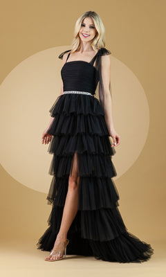 A woman in the Bow-Strap Ruffled Long Prom Ball Gown 6125, featuring tiered ruffles, a silver belt, and sheer bow shoulder straps, stands against a beige background, smiling.