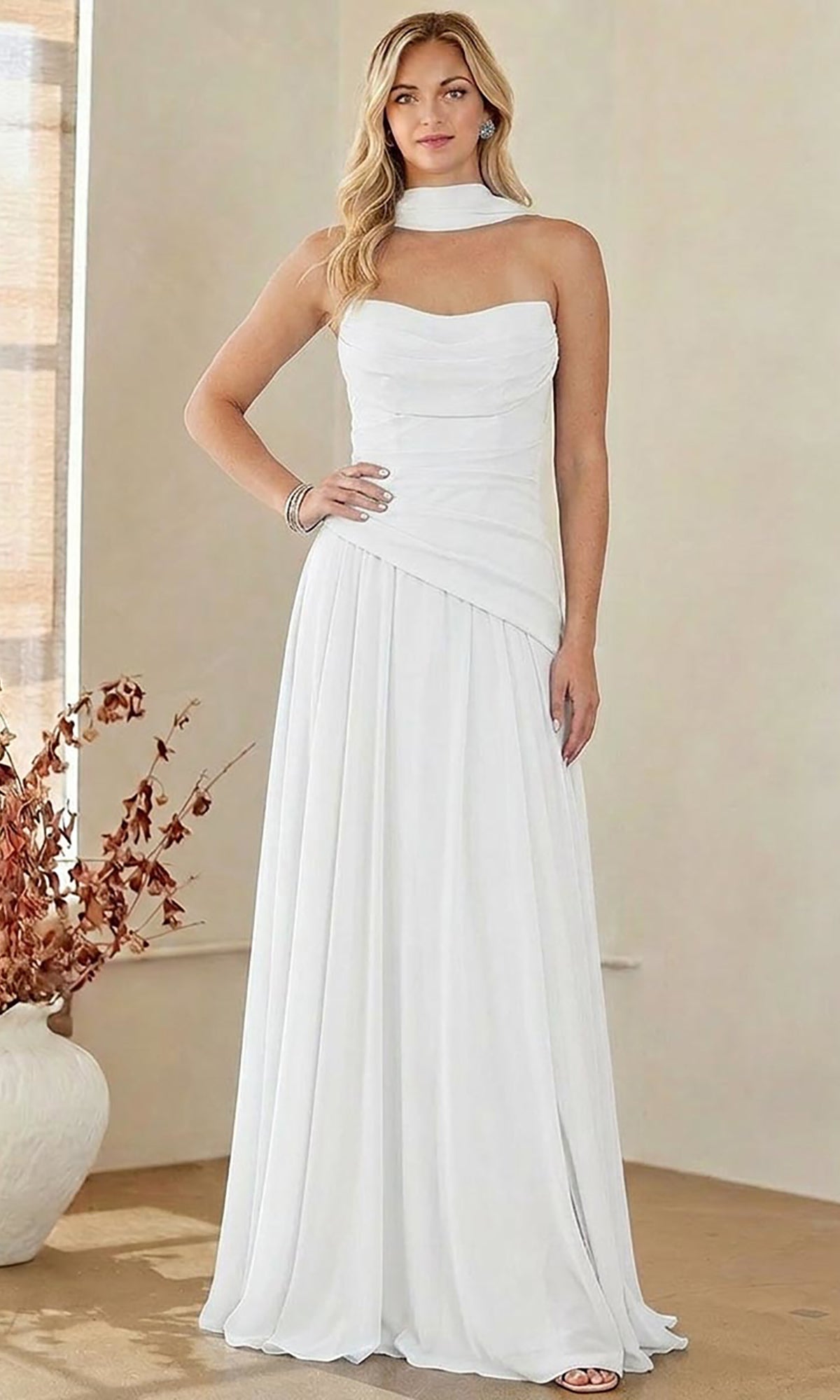 A woman stands indoors wearing the Amelia Couture 6133 Strapless Chiffon Prom Gown, a stunning white, floor-length design paired with a matching neck piece. Her long blonde hair and bracelets accentuate the elegant look of this affordable prom dress—perfect for those seeking style without compromise.