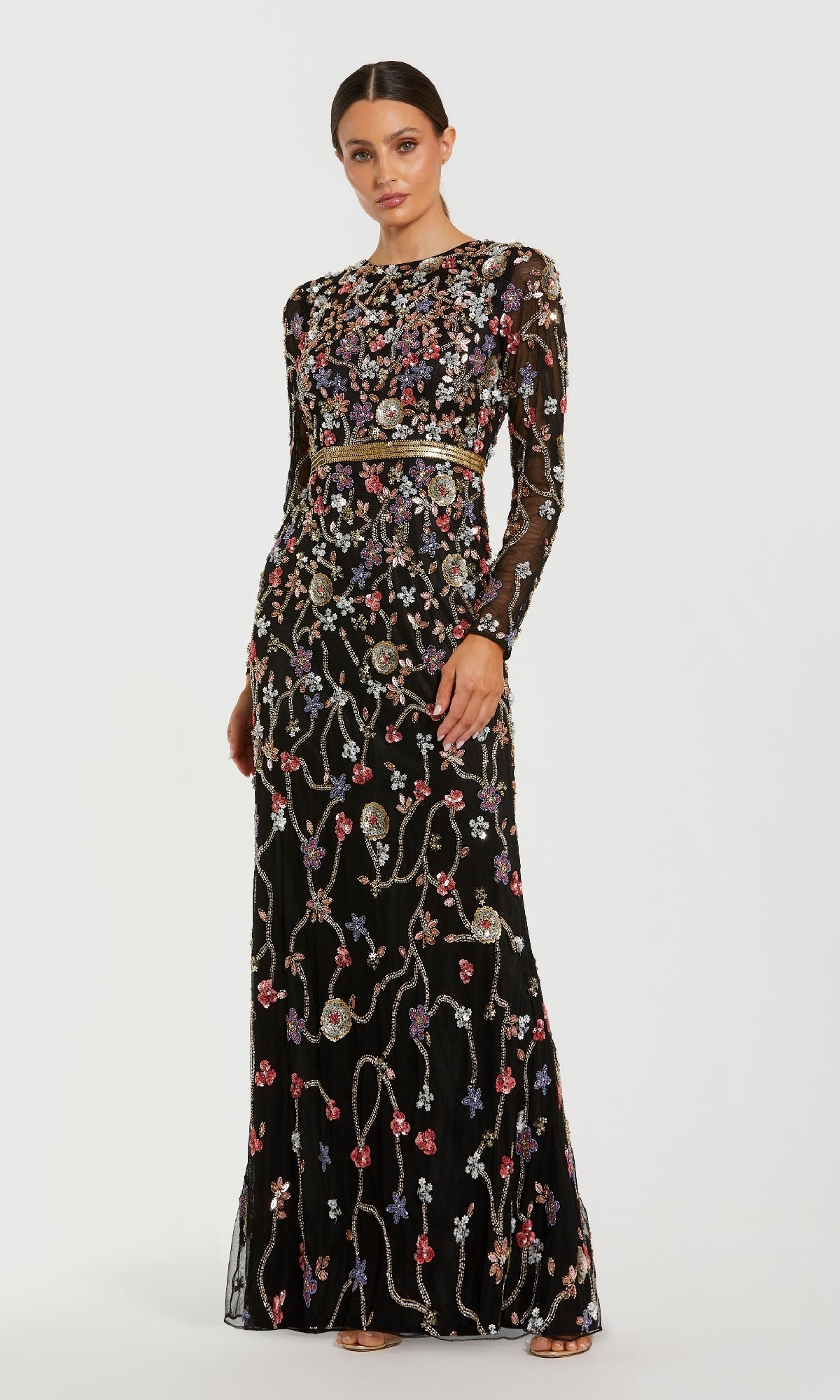 A woman wears the Mac Duggal 6135 Long Black Floral Formal Dress, featuring long sleeves, colorful floral embroidery, and beadwork, standing against a plain white background.