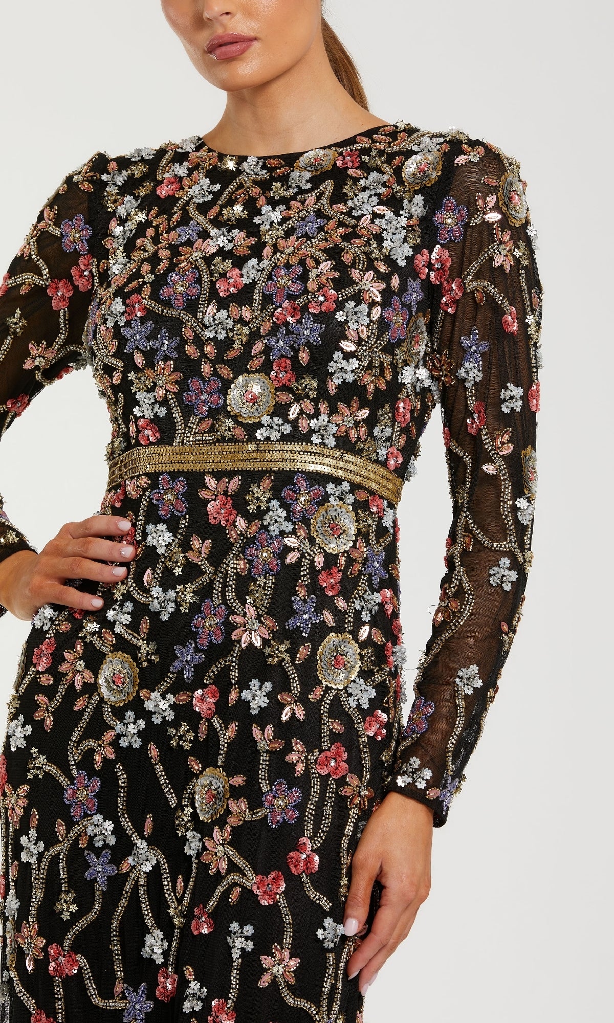 A woman poses confidently with one hand on her hip, wearing the Mac Duggal 6135 Long Black Floral Formal Dress, featuring long sleeves and colorful floral bead and sequin embroidery.