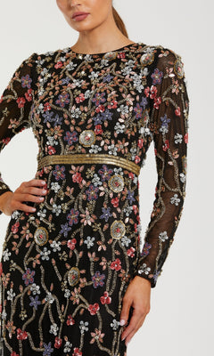 A woman poses confidently with one hand on her hip, wearing the Mac Duggal 6135 Long Black Floral Formal Dress, featuring long sleeves and colorful floral bead and sequin embroidery.