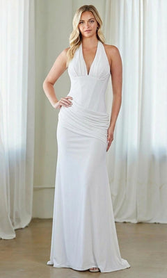 A woman stands indoors wearing the Amelia Couture 6150, a sleeveless white floor-length formal dress with a halter neckline and ruched waist. White curtains are in the background.